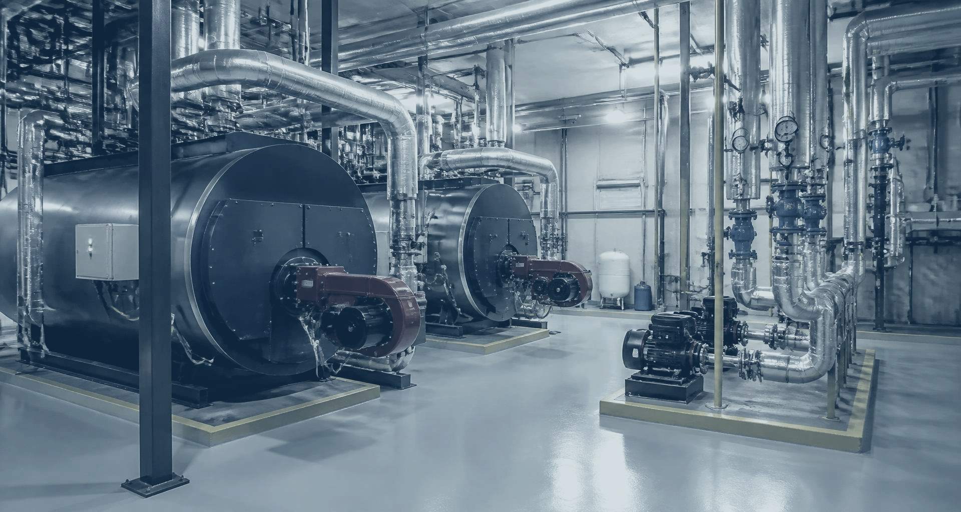 A commercial plant room with two boilers, insulated pipework runs, circulation pumps and valves set out on a painted floor.